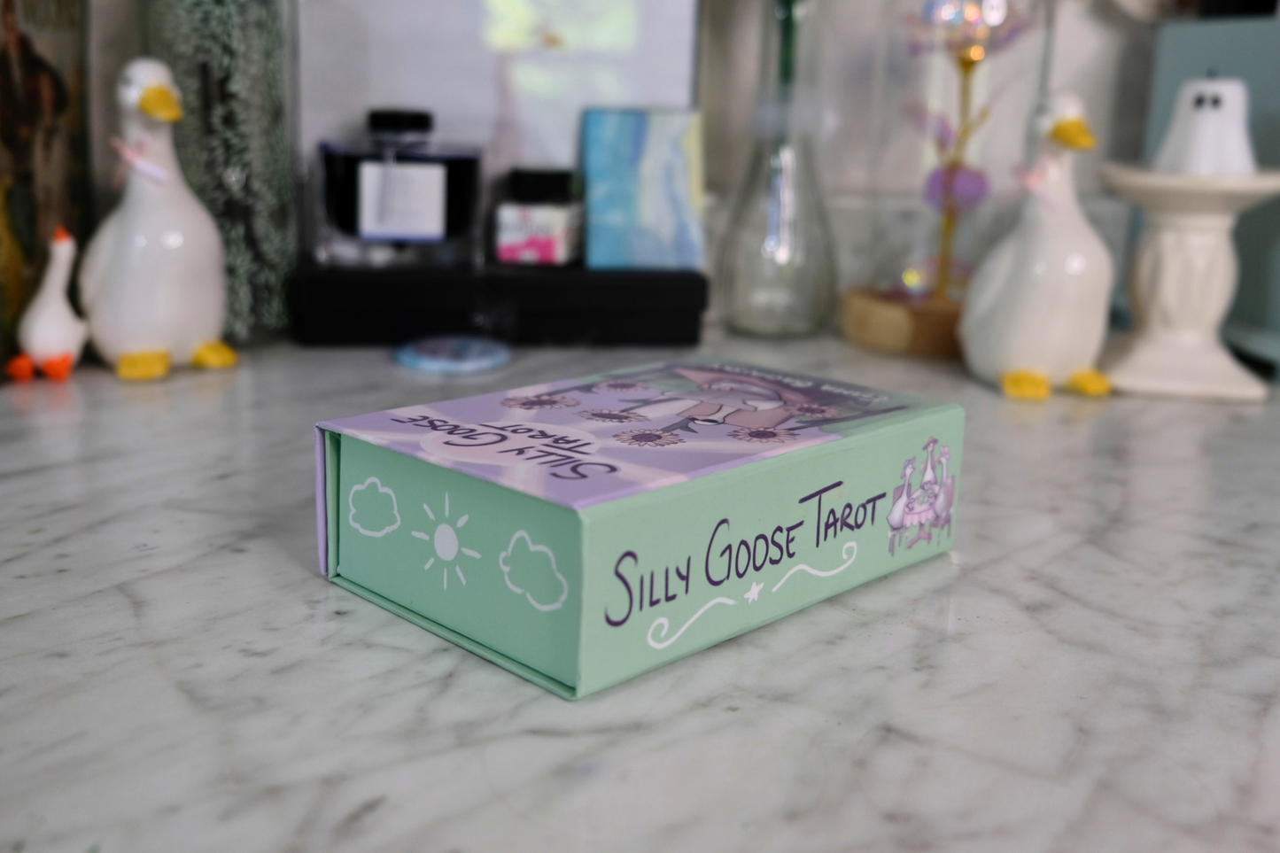 Silly Goose Tarot box on a marble surface with decorative items in the background