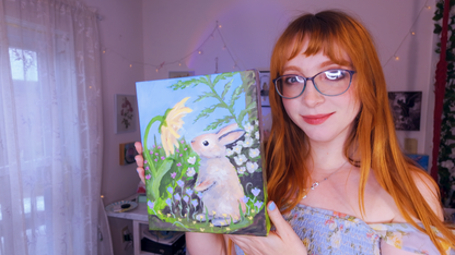 Artist Emma Baginsky holding a painting of a rabbit in a room with white curtains.