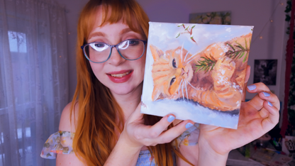 Artist Emma Baginsky holding a painting of a cat, smiling at the camera.